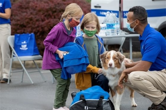Two masked girls and their dog with a masked emergency services worker