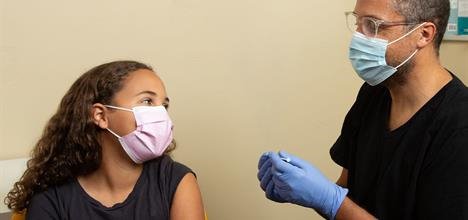 Masked teenager talking with masked and gloved clinician