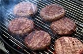 Photo of charcoal grill with five grill marked, smoking hamburgers.