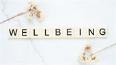 "Wellbeing" spelled with Scrabble letters on marble background with two flowers 
