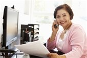 Office setting-desk-computer- smiling Hispanic woman on phone.