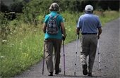 Photo of elderly man and woman walking on a path using hiking sticks.