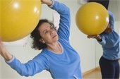 Older Latina woman exercising with large yellow exercise ball.