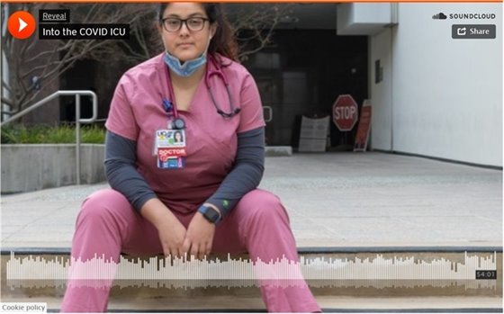 Woman doctor sitting in pink scrubs, with mask pulled down below chin